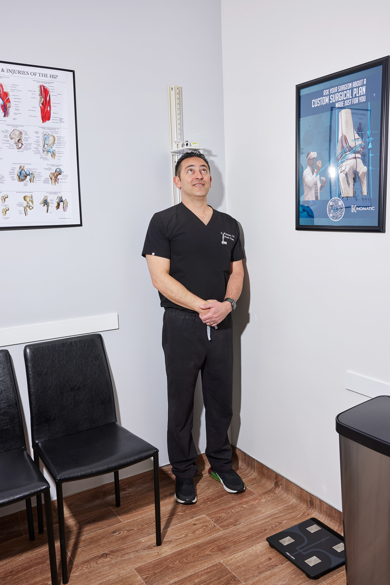 A man in scrubs stands against a height-measurement device