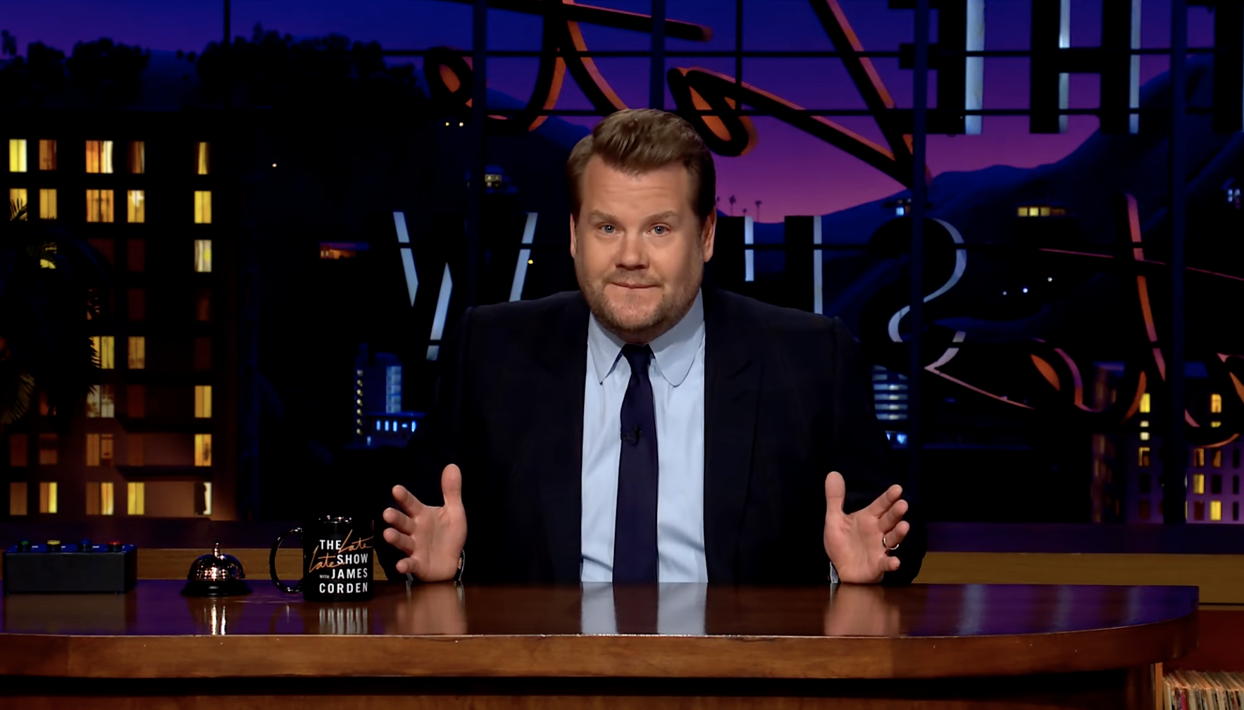 James behind his desk on the set, gesturing with his hands