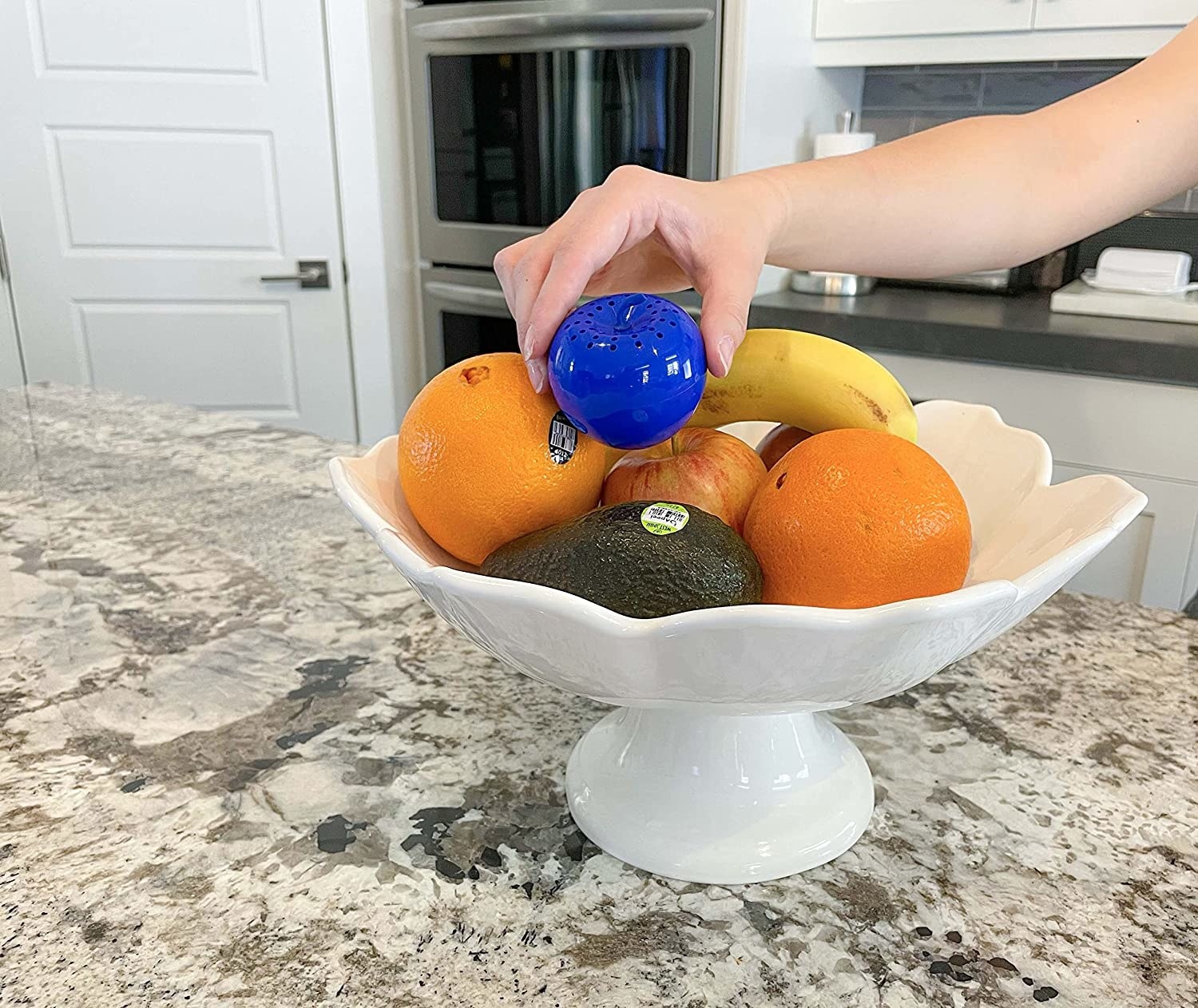 person placing the bluapple into a bowl of fruit
