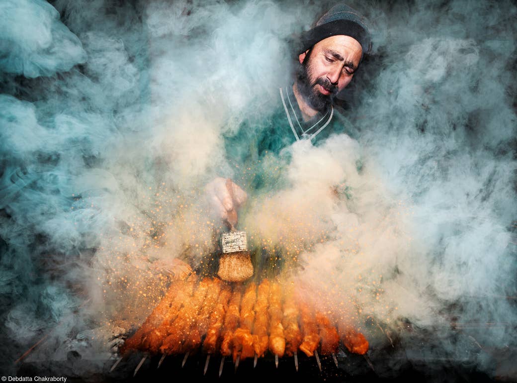 A man calmly cooks kebabs on skewers while surrounded by smoke