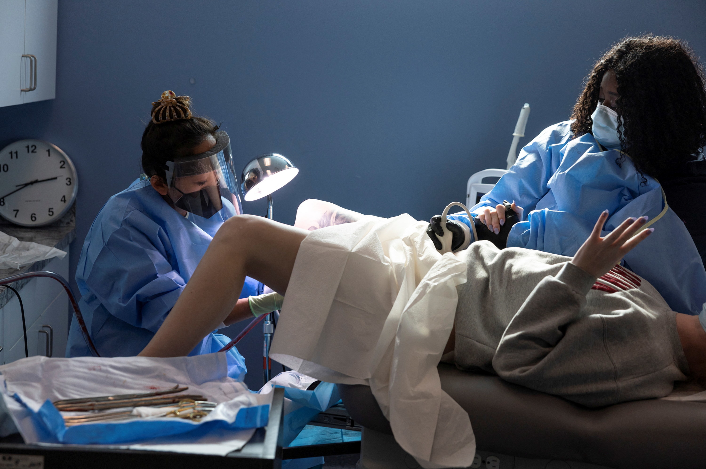Two people in surgical gowns and masks work on a patient