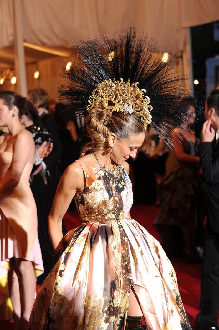 SJP in a gold and feather faux hawk hat and gown with a middle slit