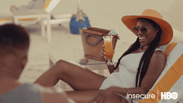 a gif of actress Yvonne Orji in &quot;Insecure&quot; in a bathing suit, on a chaise lounge, holding a drink, and stroking her hair