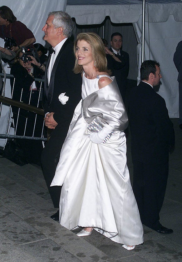 Caroline wears a long oversized shiny coat over her dress