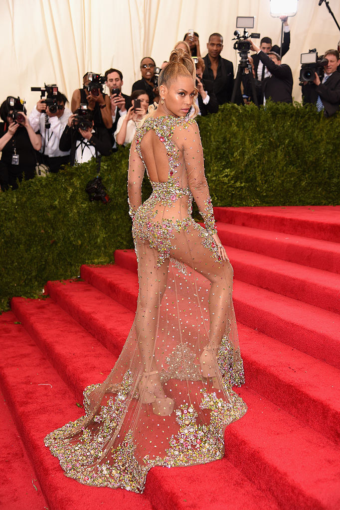 Beyonce wears a sheer dress with a train that has jeweled detailing along the bottom