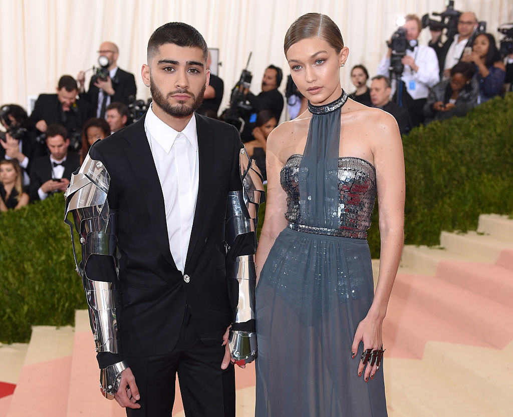 Zayn wears a suit with metal armor detailing for the sleeves and Gigi wears a long silver dress with shiny detailing for the top