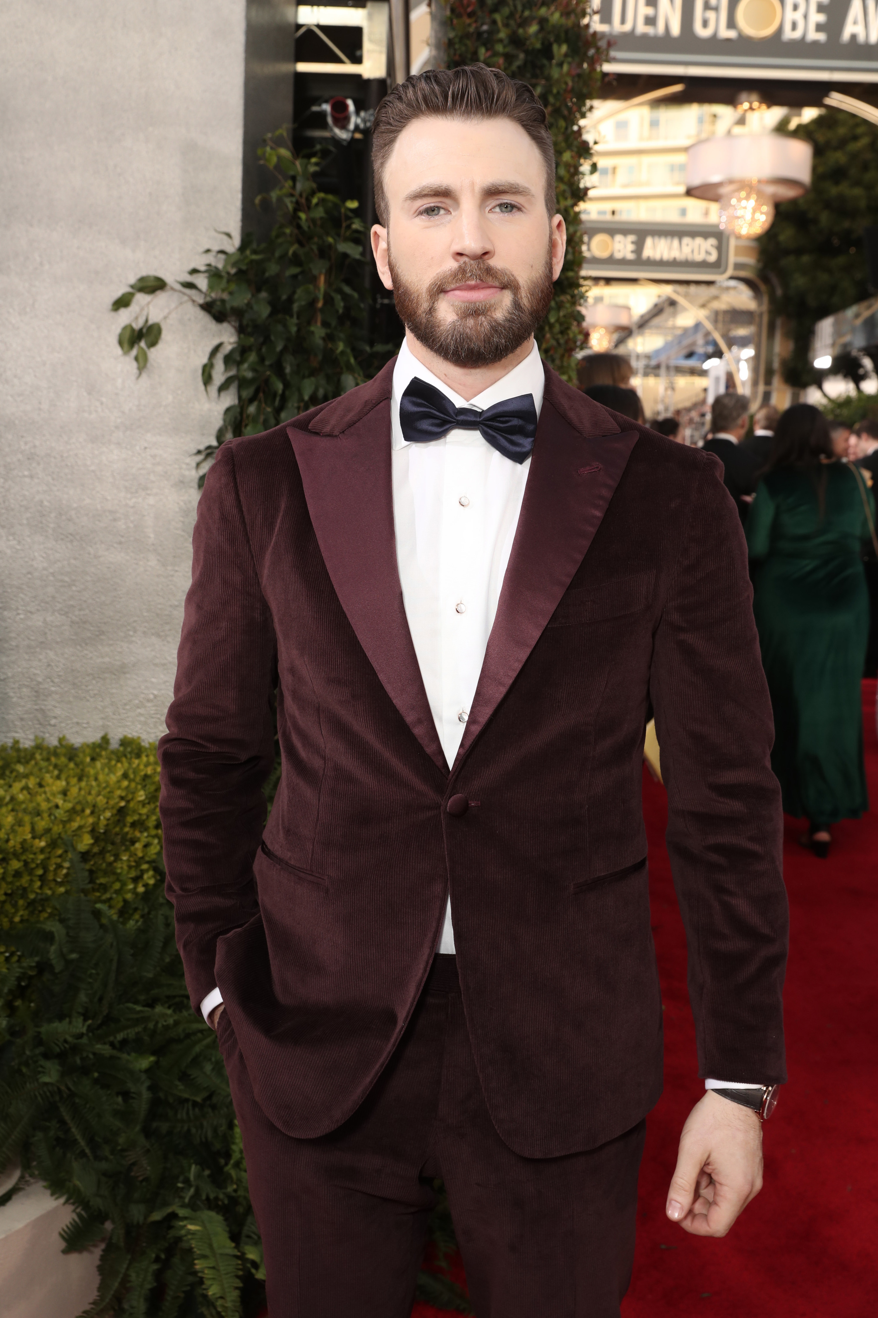 Chris poses with his hand in his pocket while wearing a suit