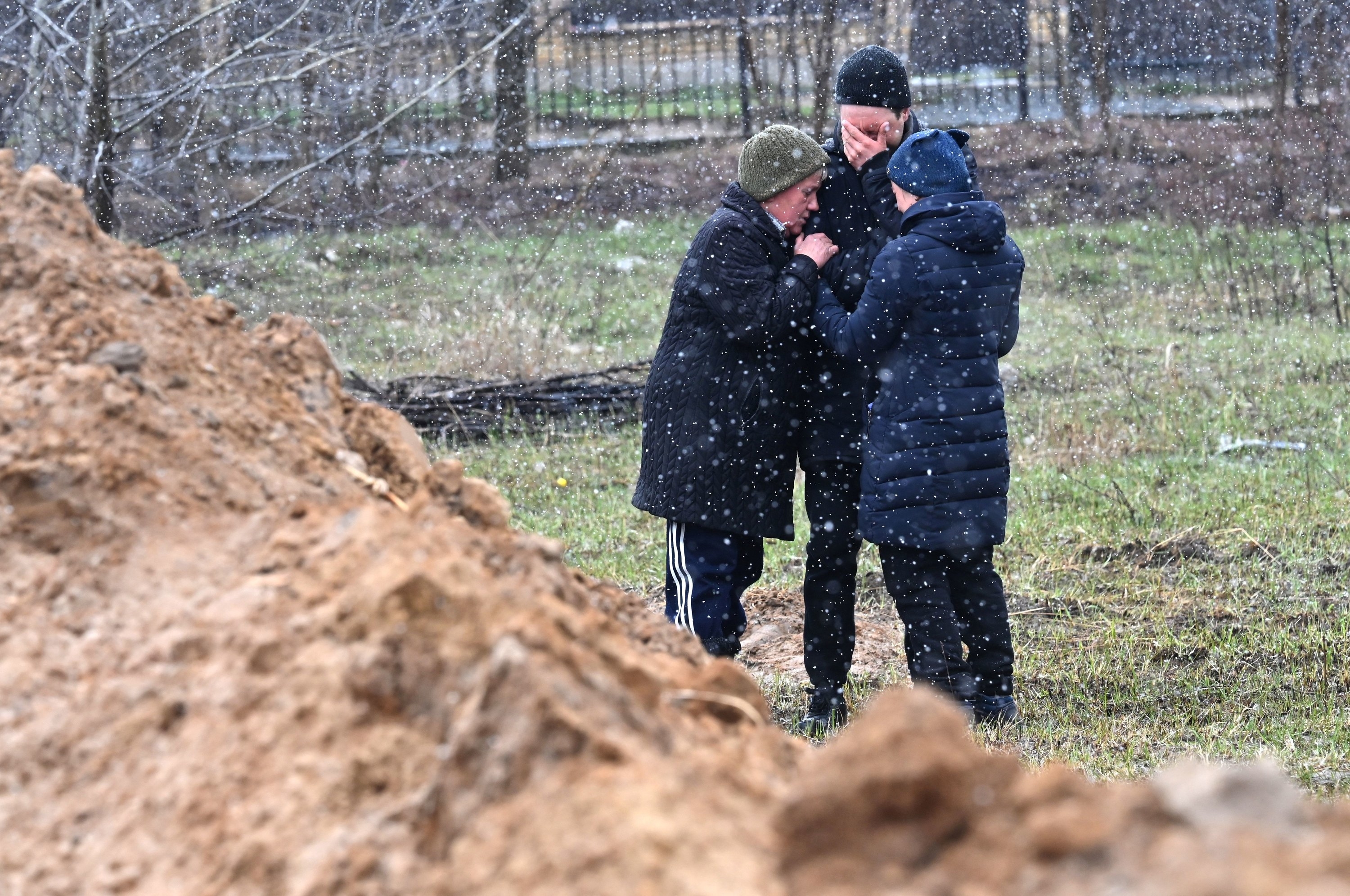 Three people stand together, with one man covering his face with his hand