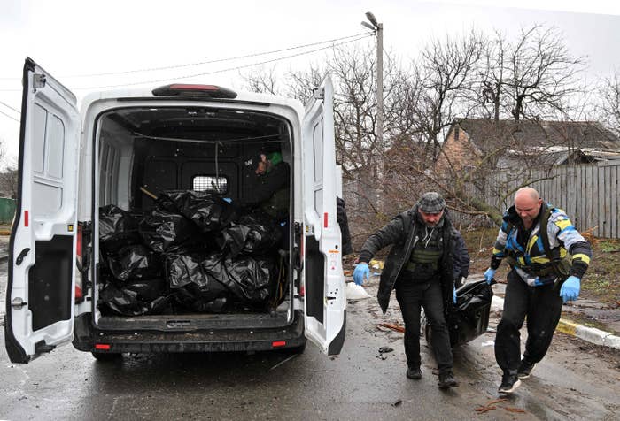 Two men drag a body bag toward a truck filled with body bags