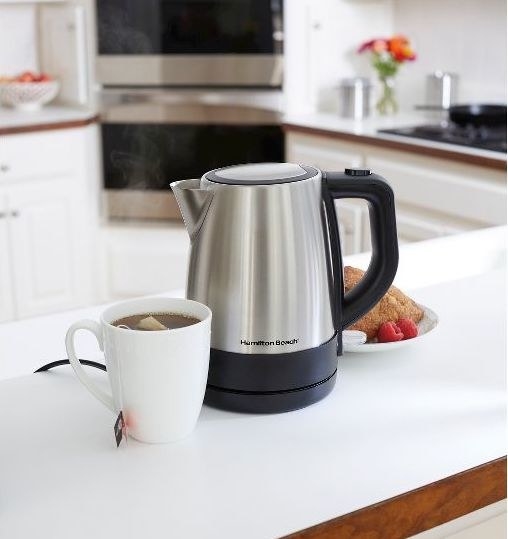 stainless steel electric kettle on a counter next to a cup of tea