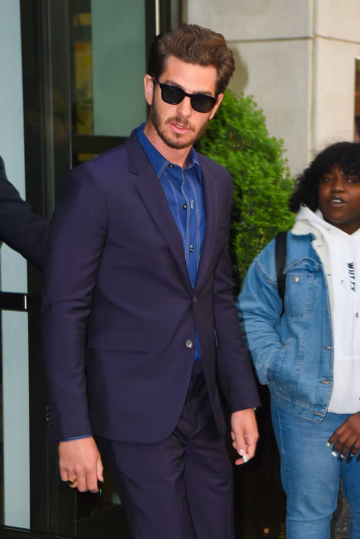 Andrew steps out of a building while wearing a suit and shades