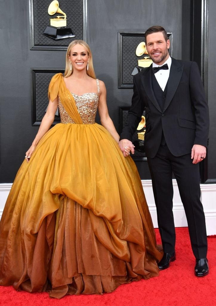 Smiling Carrie in a long princess gown and holding hands with John, who&#x27;s wearing a bow tie