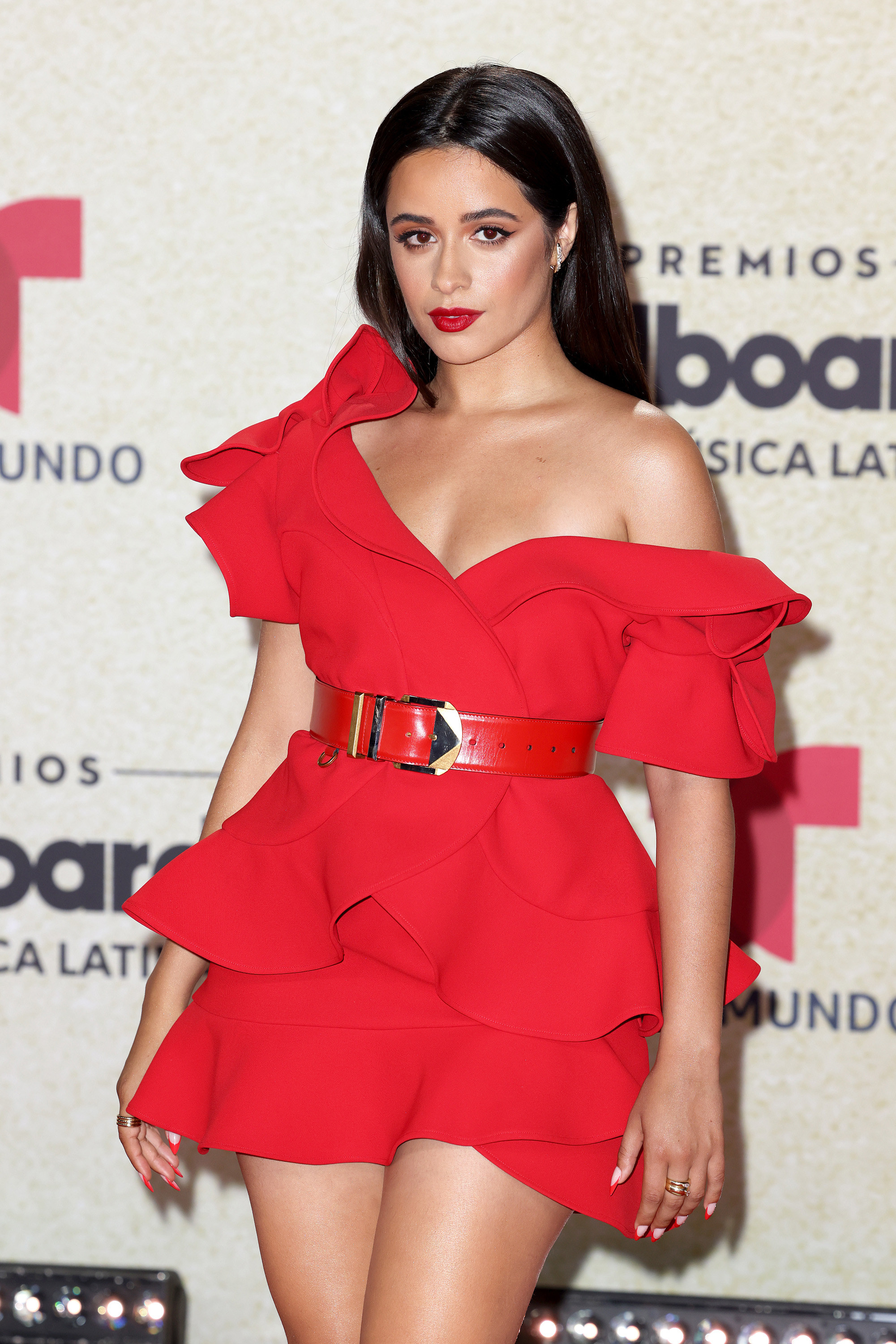 Camila on the red carpet in a bright-colored short, frilly dress with belt