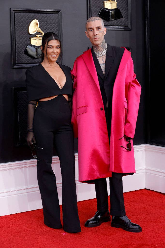 Kourtney in a plunging V-neck pantsuit with Travis in a trench coat