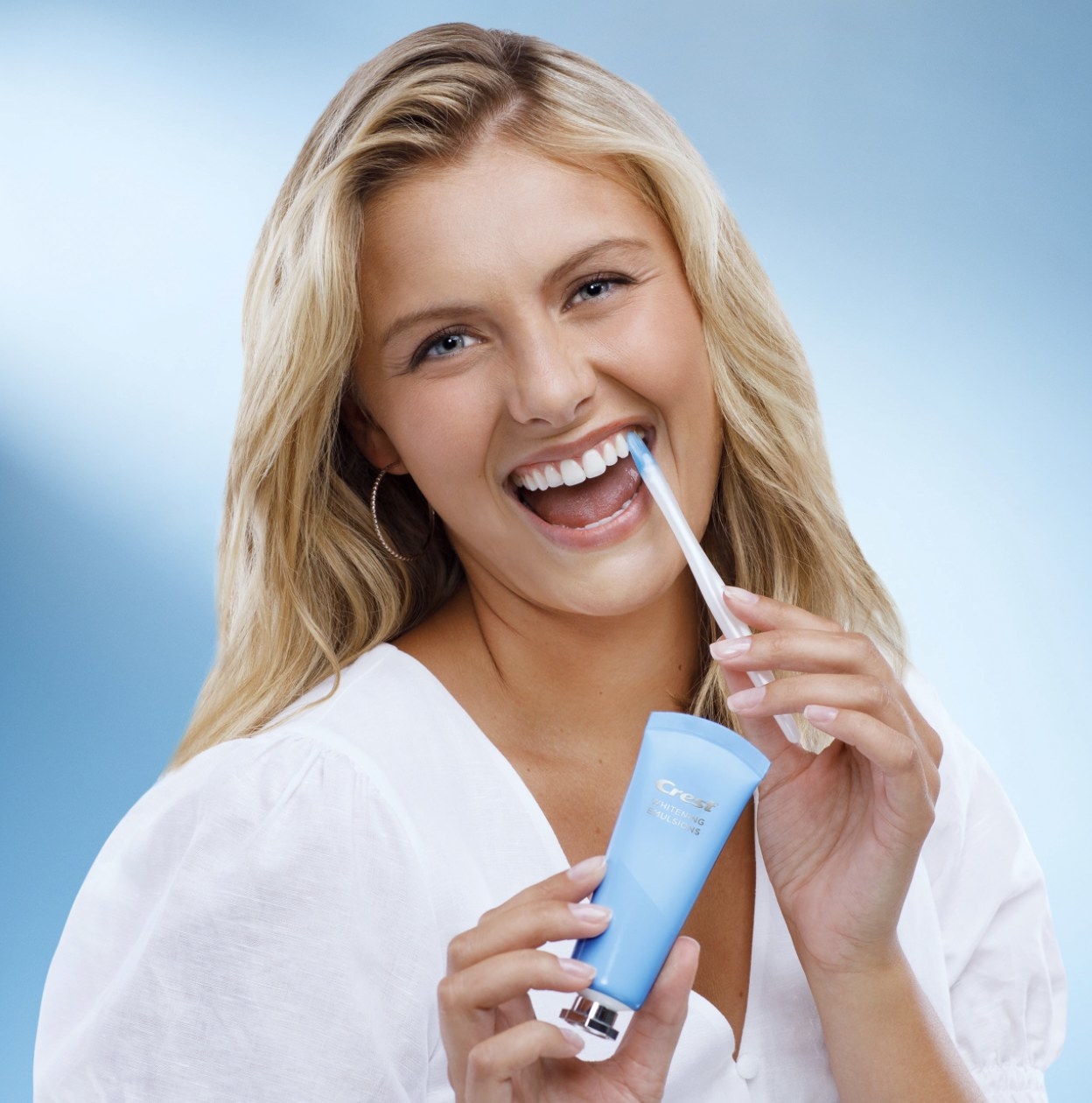 Model using the wand on her white teeth and holding the tube of whitening treatment