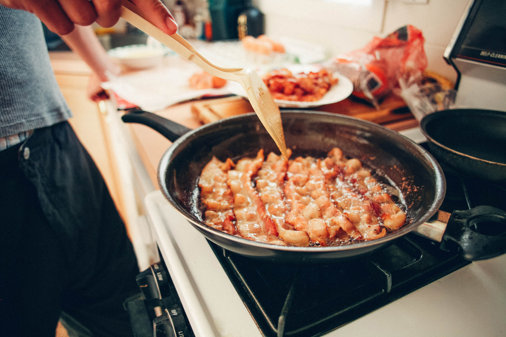 A man making bacon in a frying pan.