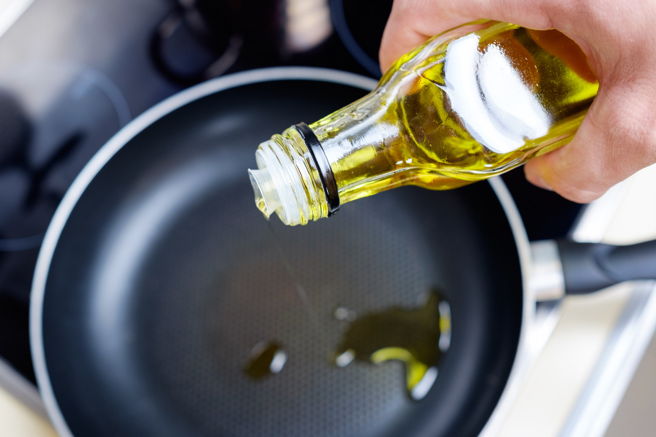 Pouring oil from a bottle into a skillet.