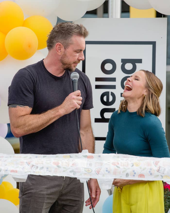 Dax Shepard holding a microphone and looking at a smiling Kristen Bell