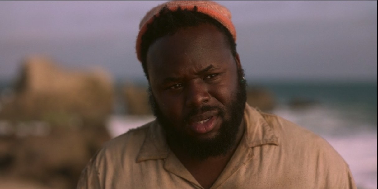 Oluwande stands on a beach looking lovingly at his friend.