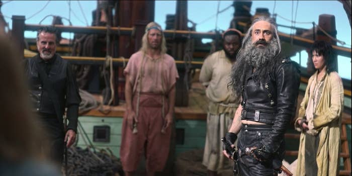 A group of five pirates, four in the background. A leather-clad pirate with long hair and a beard stands in the front.