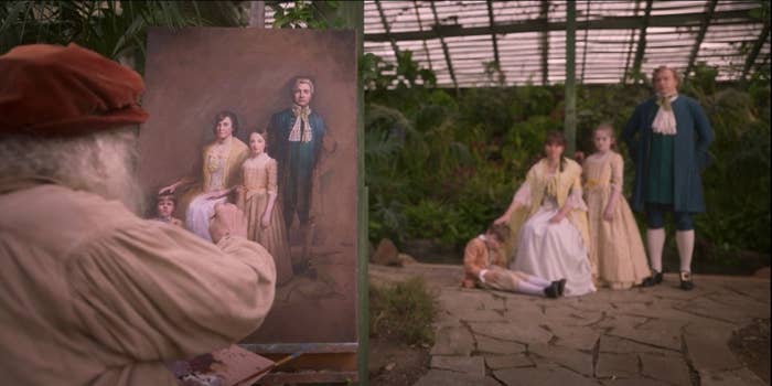 A painter sits in front of a canvas, where he's painting an image of a well-dressed white family consisting of a small boy on the ground, his mother in a chair, a young girl standing behind her, and the father standing to her side.