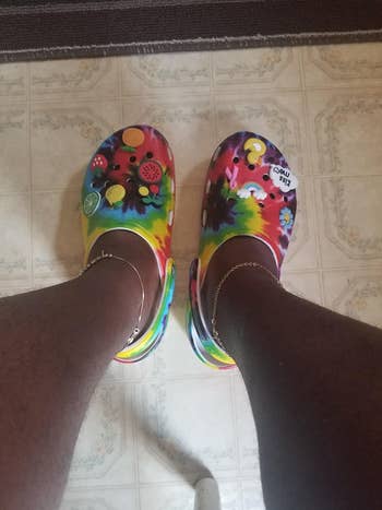 reviewer wears rainbow tie-dye Crocs with cute personalized charms on front