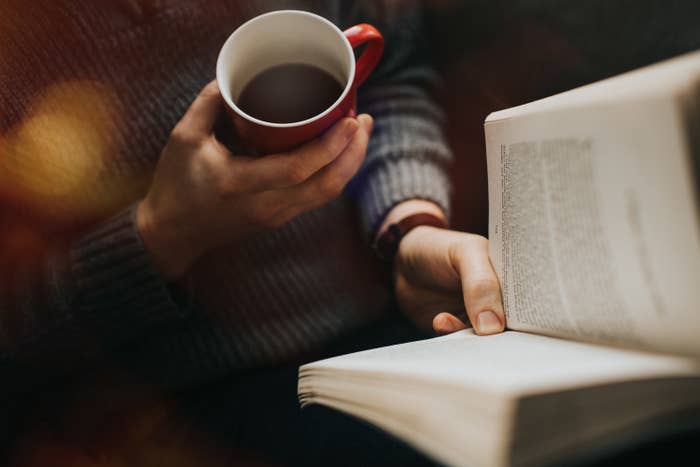 person's hand holding coffee and other hand reading a book
