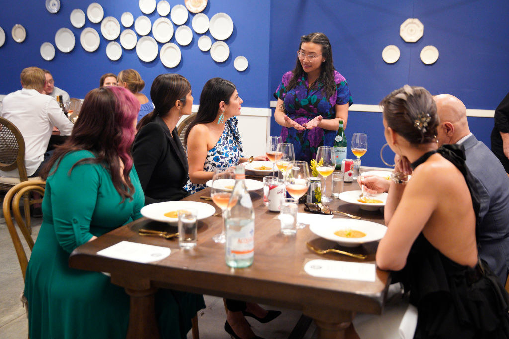 A woman speaking to a group of people at the dinner table.