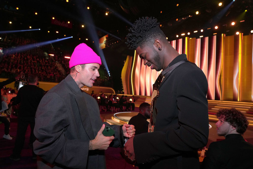 Justin in a boxy suit holds up his hand next to Lil Nas