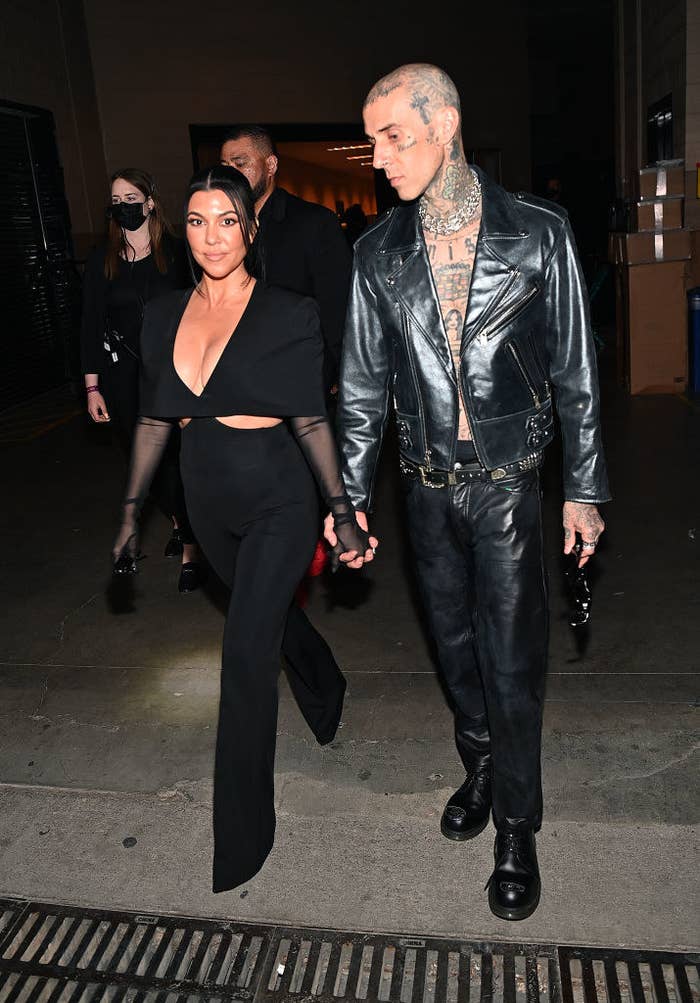 Kourtney in a low-cut top and pants and bare-chested Travis in a leather suit