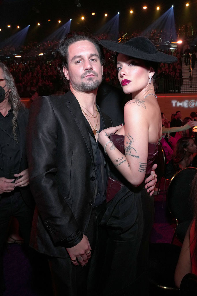 Alev in a shiny, bare-chested suit hugs Halsey in a wide-brimmed hat and strapless dress