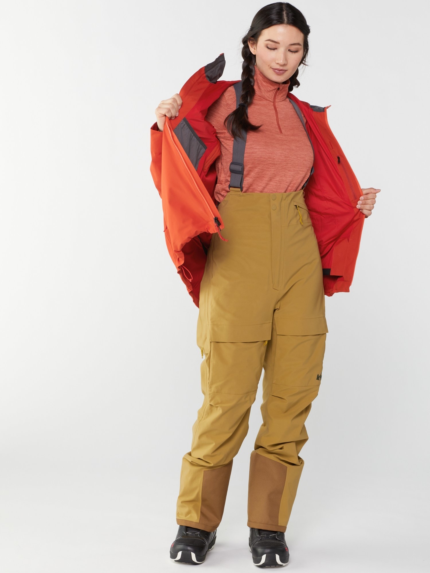 Model wearing the orange ski jacket over base layers and ski bibs