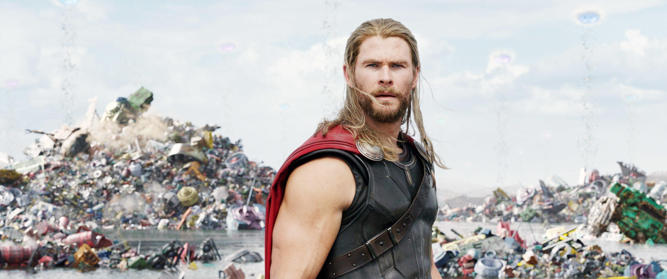 A close up of Thor was long hair as he stands in the middle of a dump