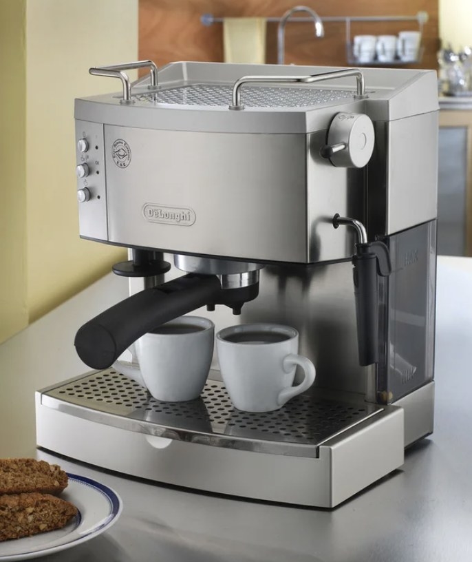 The silver espresso maker has black handles and two white espresso mugs