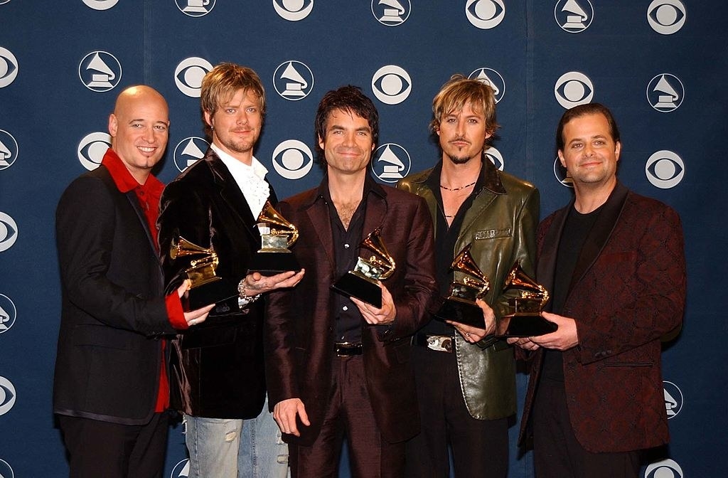 Five members, each holding a Grammy, wearing jackets, no ties