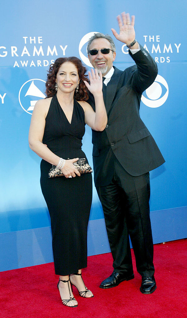Both waving and smiling, Gloria in a halter, ankle-length, straight-line dress and Emilio in a suit