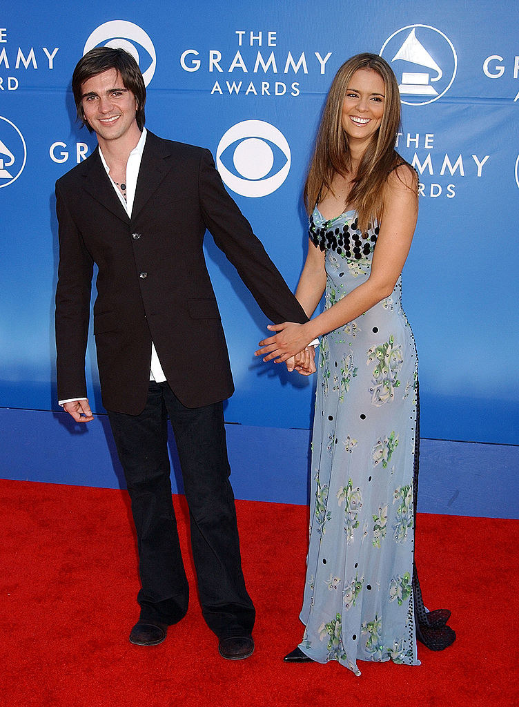 They&#x27;re holding hands and she&#x27;s wearing a long straight, flowery gown; he&#x27;s in a suit, no tie