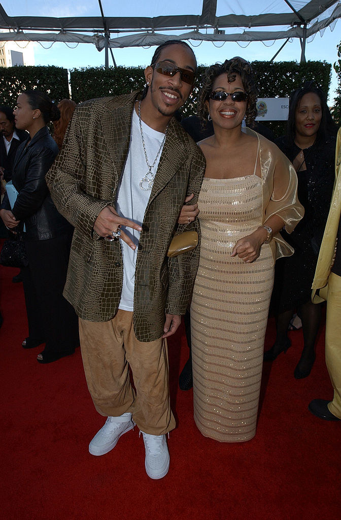 Ludacris wearing a loose jacket and loose pants and Gladys wearing a long, tiered gown with spaghetti straps and shoulder wrap