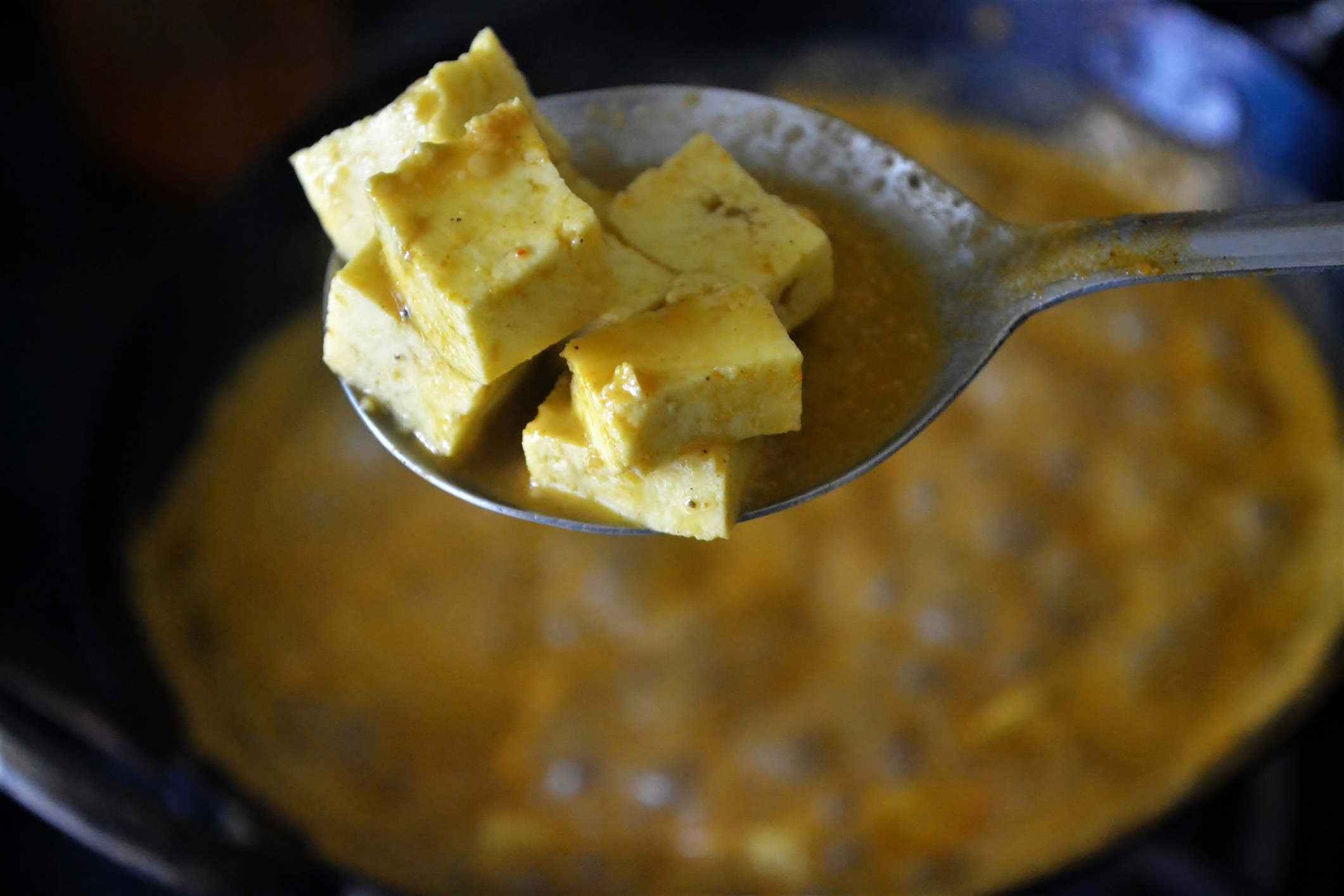 A spoon holding pieces of Indian paneer cheese