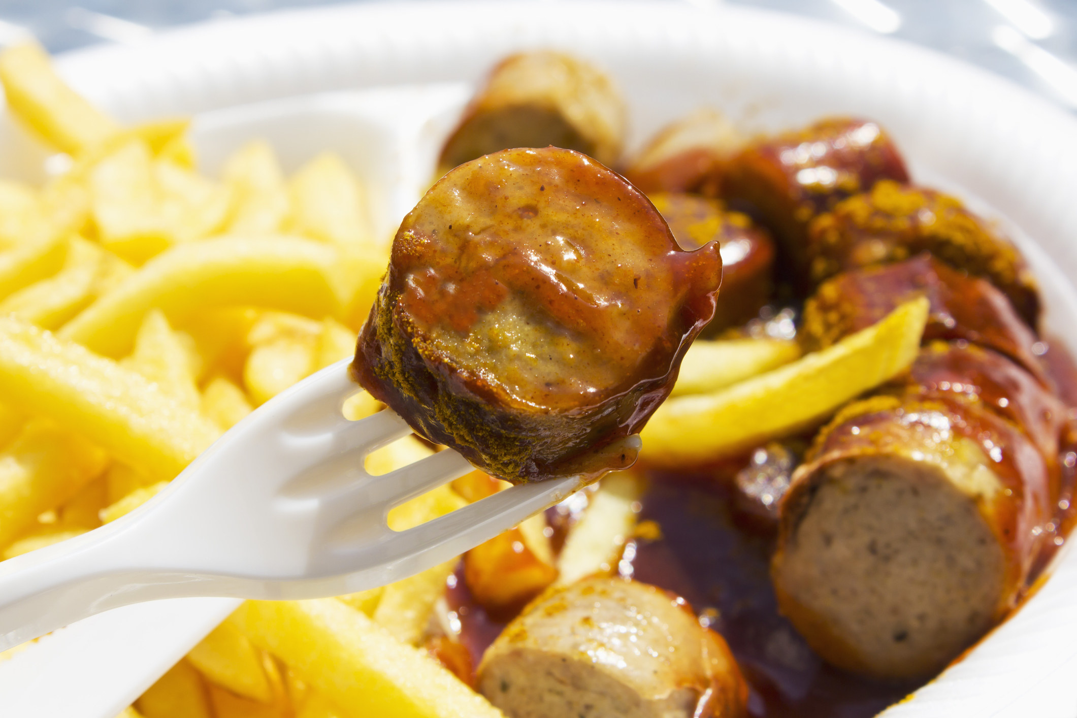 Curry sausage on a fork with french fries in the background