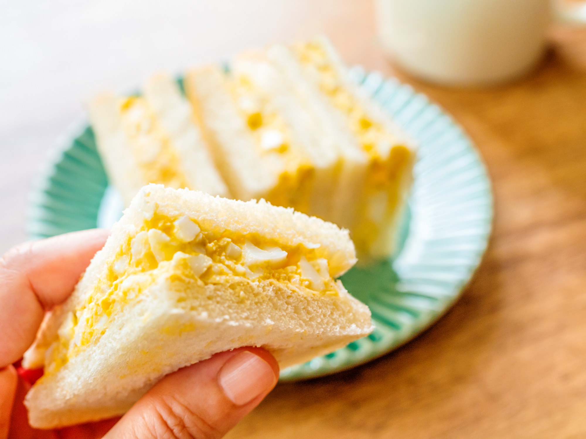 A hand holding a slice of a Japanese egg salad sandwich