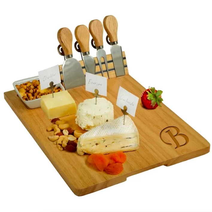 Wooden board with cheese knives, cheese, fruit and nuts