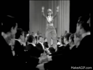 woman in top hat jumps into the arms of rows of men