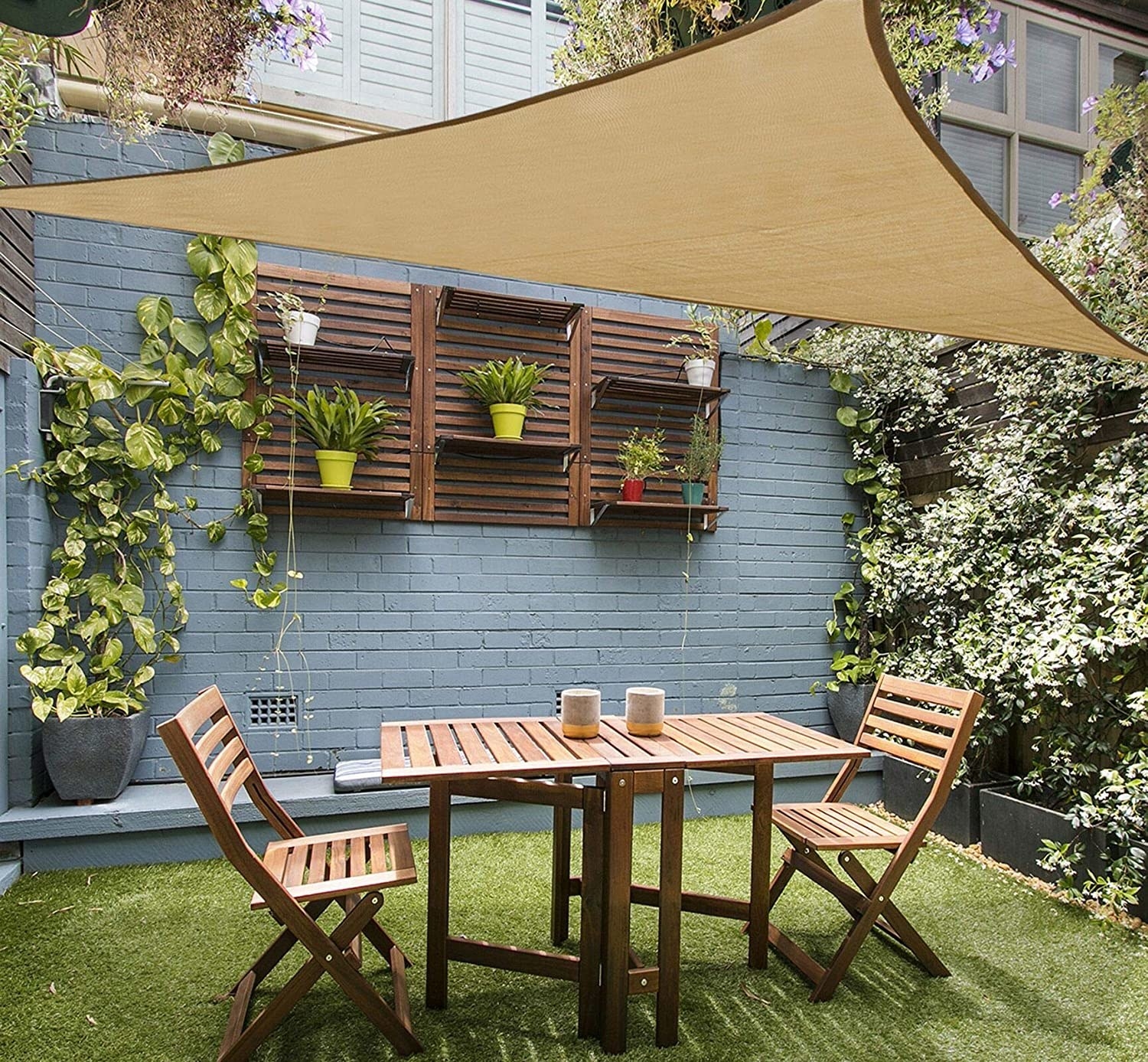 tan sunshade triangle above wooden table and chairs set on patio with faux grass