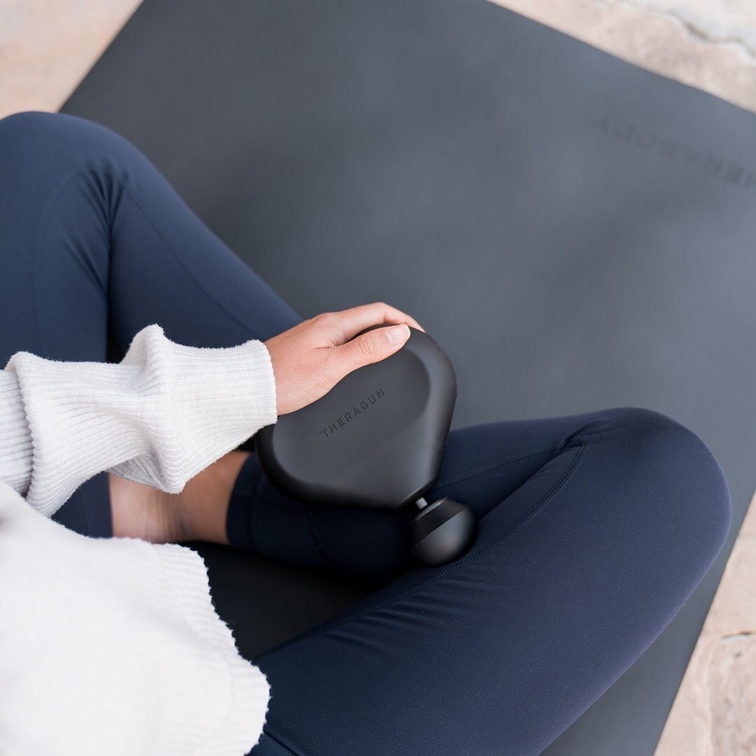 A person using the massager on their leg while sitting on a yoga mat
