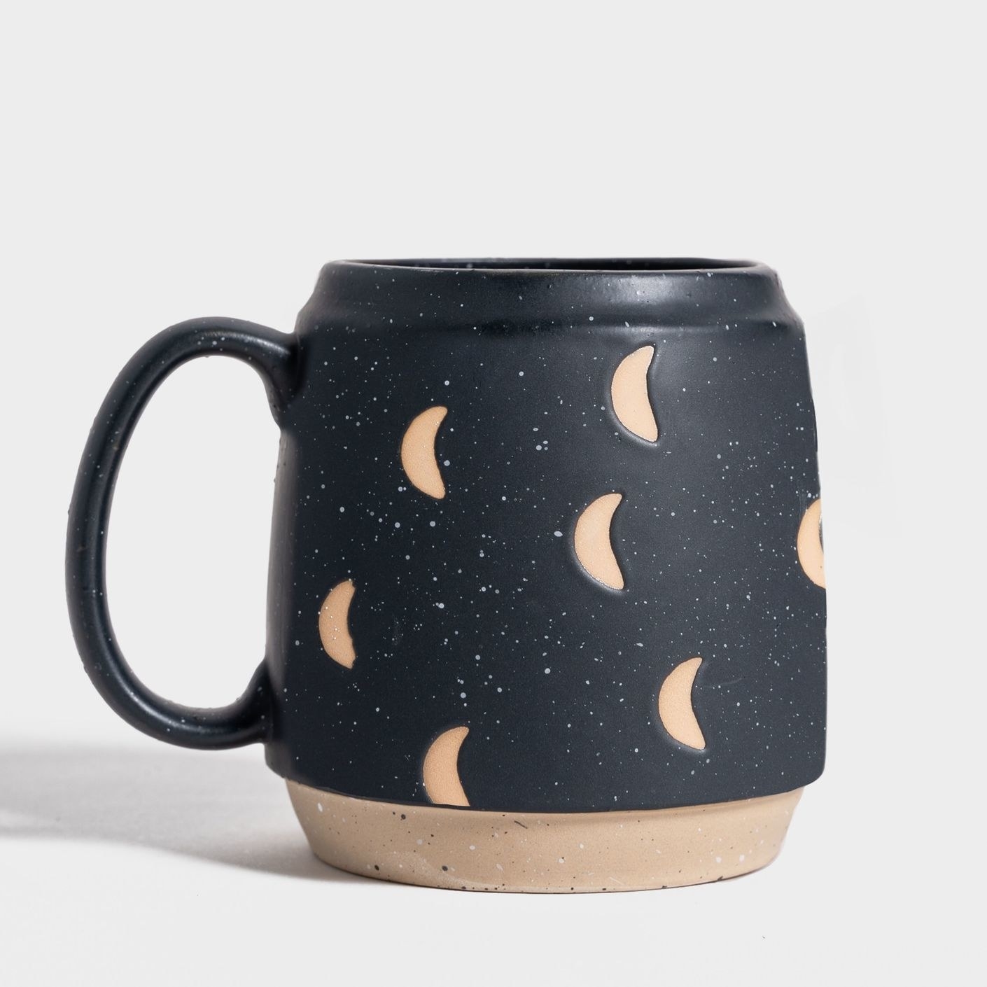stoneware barrel-shaped mug with a black speckled glaze and an unglazed crescent moon pattern