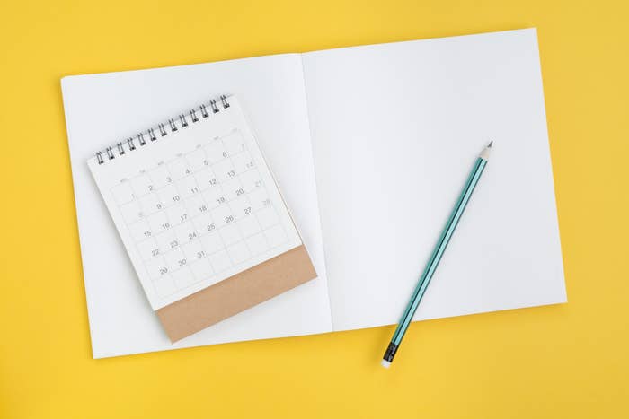 A blank notebook, calendar, and pencil all sit on a flat surface