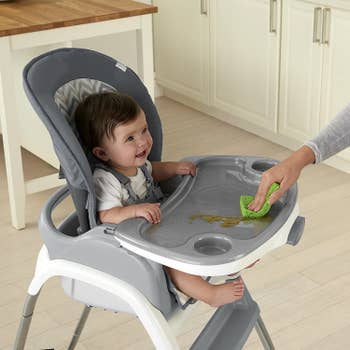 A hand wiping the high chair tray while a baby smiles