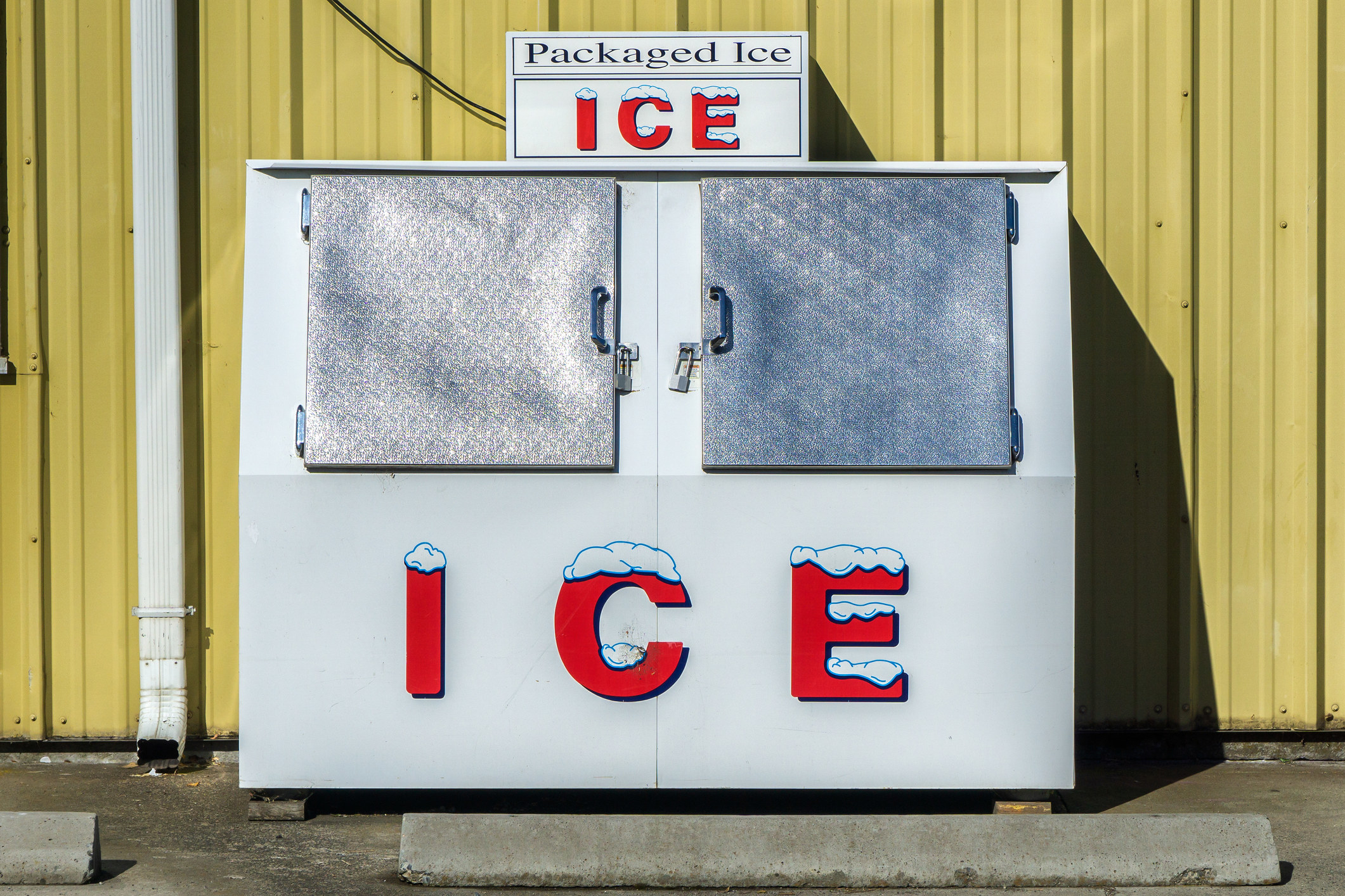 Packaged Ice freezer machine against a yellow wall during a hot and sunny day of summer outside a grocery store