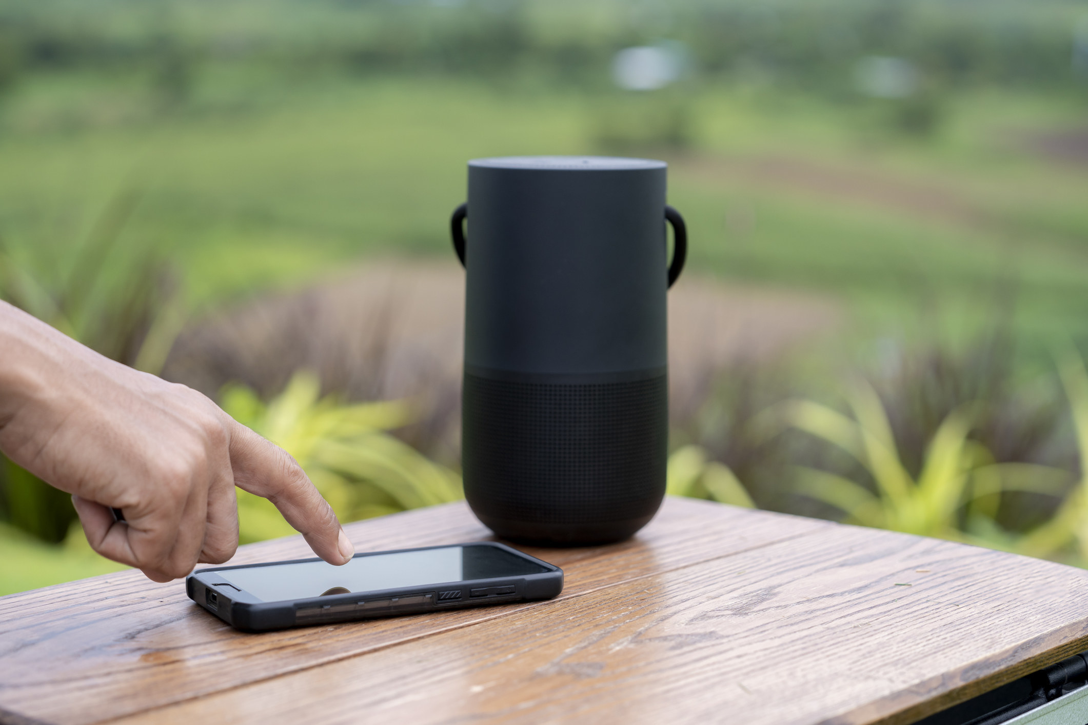 Hand touches a screen on smartphone with portable speaker outdoors